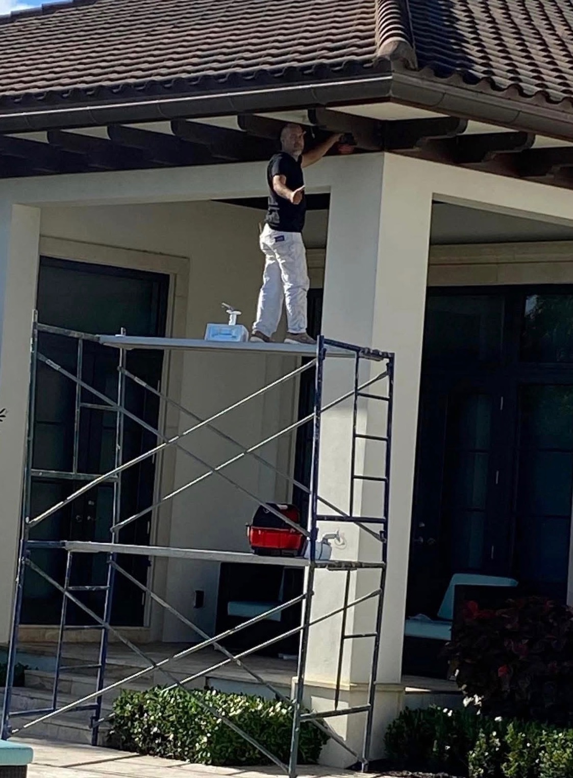 Painter working from a scaffold platform under a tile roof