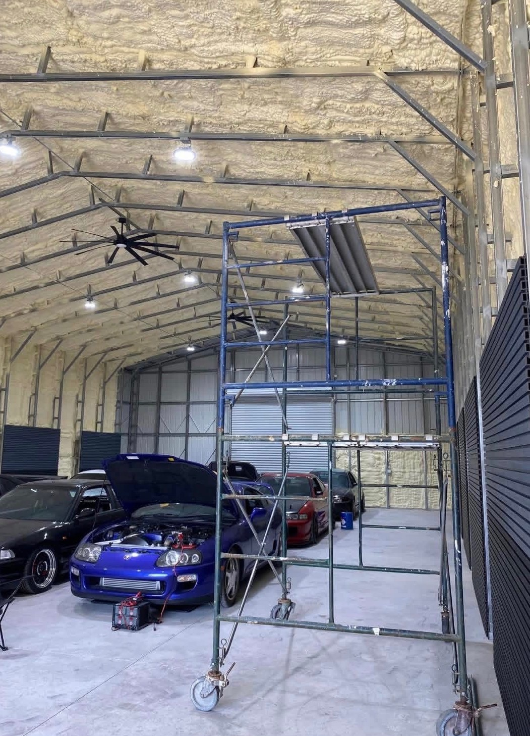 Scaffold tower inside a high-ceiling warehouse with cars